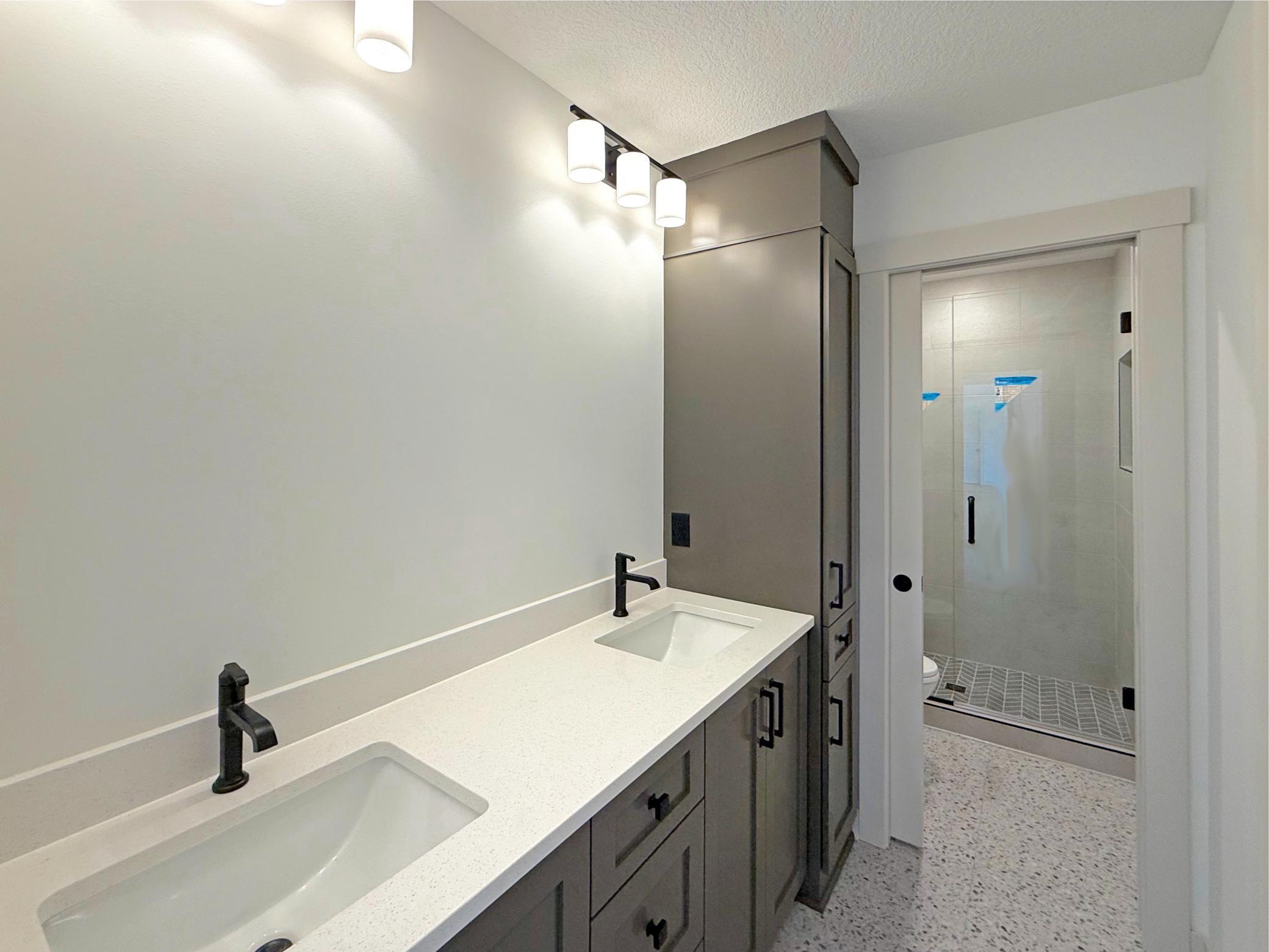 Contemporary finishes define this spacious full bathroom, complete with a custom double vanity, designer fixtures, and a sleek tiled walk-in shower that complements the home's upscale style.