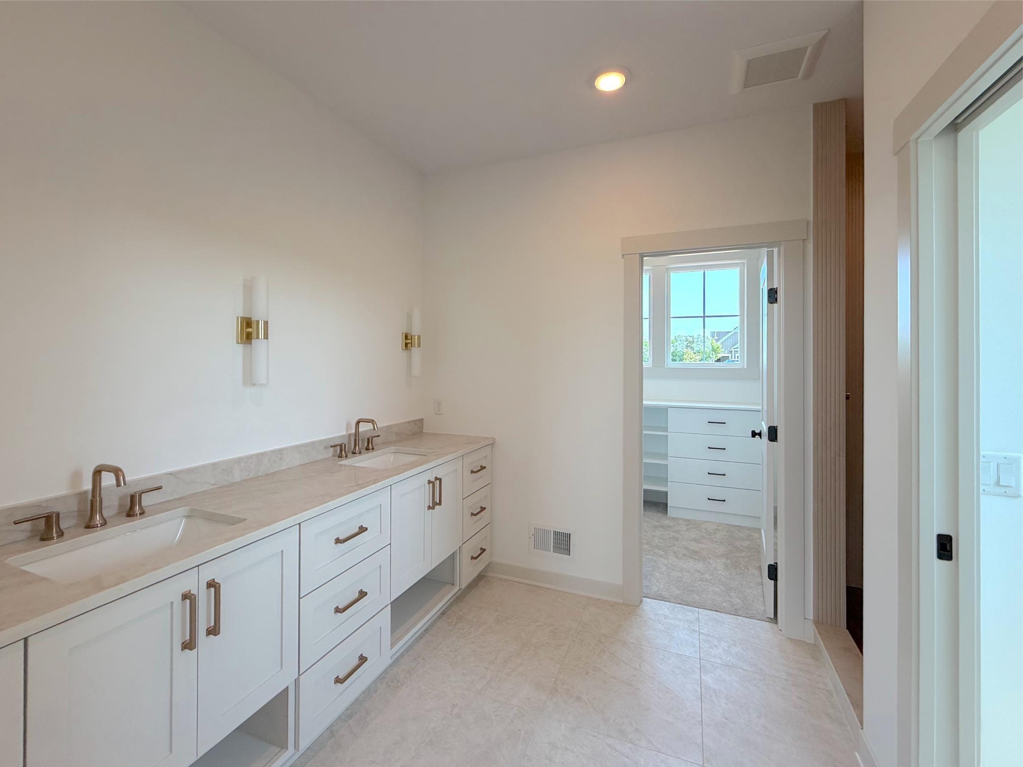 The thoughtfully designed primary bathroom features a spacious dual-sink vanity with quartz countertops, bright custom cabinetry & flooring, soft lighting and elegant finishes.