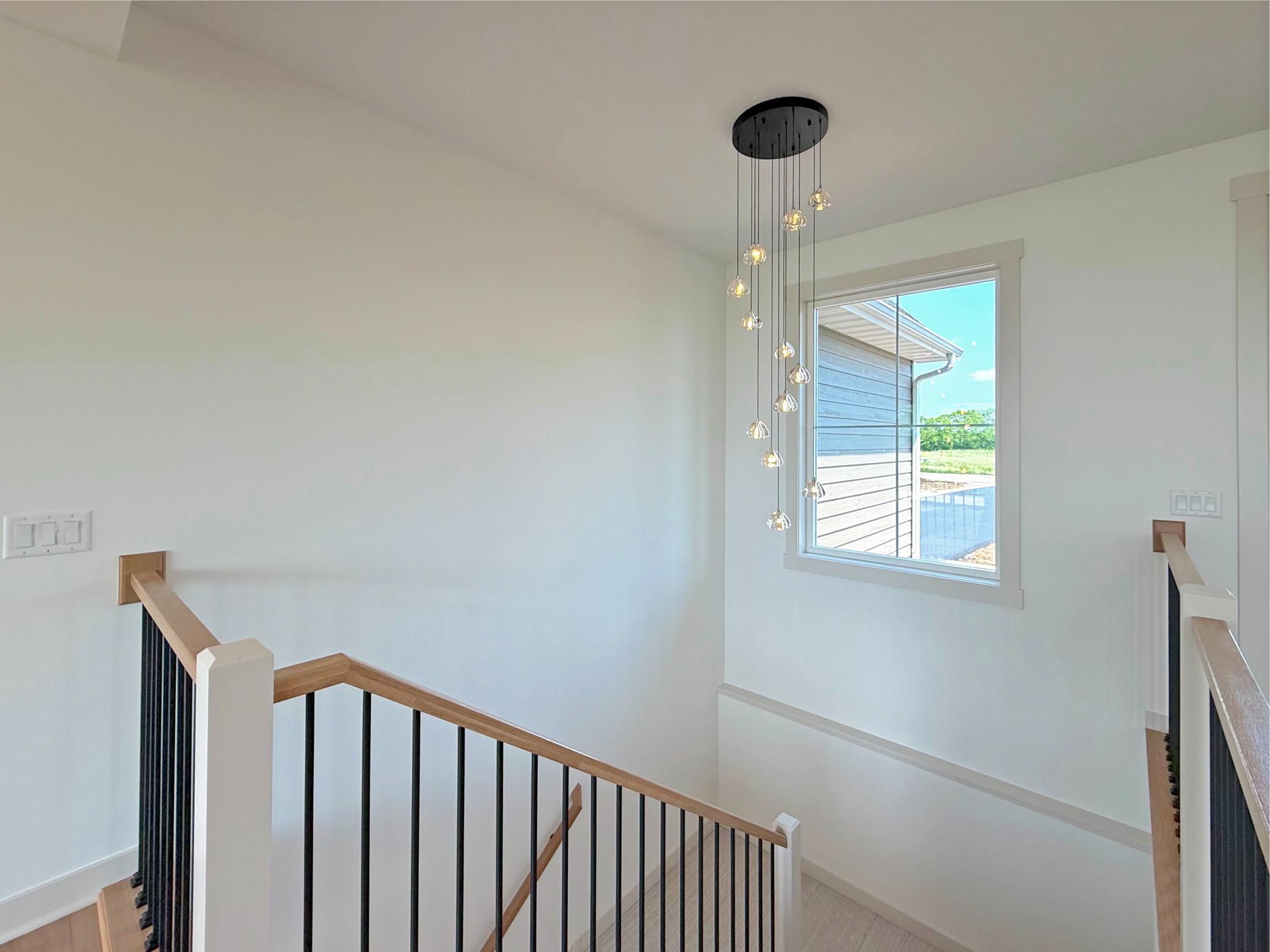The open staircase makes a striking architectural statement with sleek iron balusters, warm wood handrails, and a designer cascading pendant that elegantly connects the home's two levels.