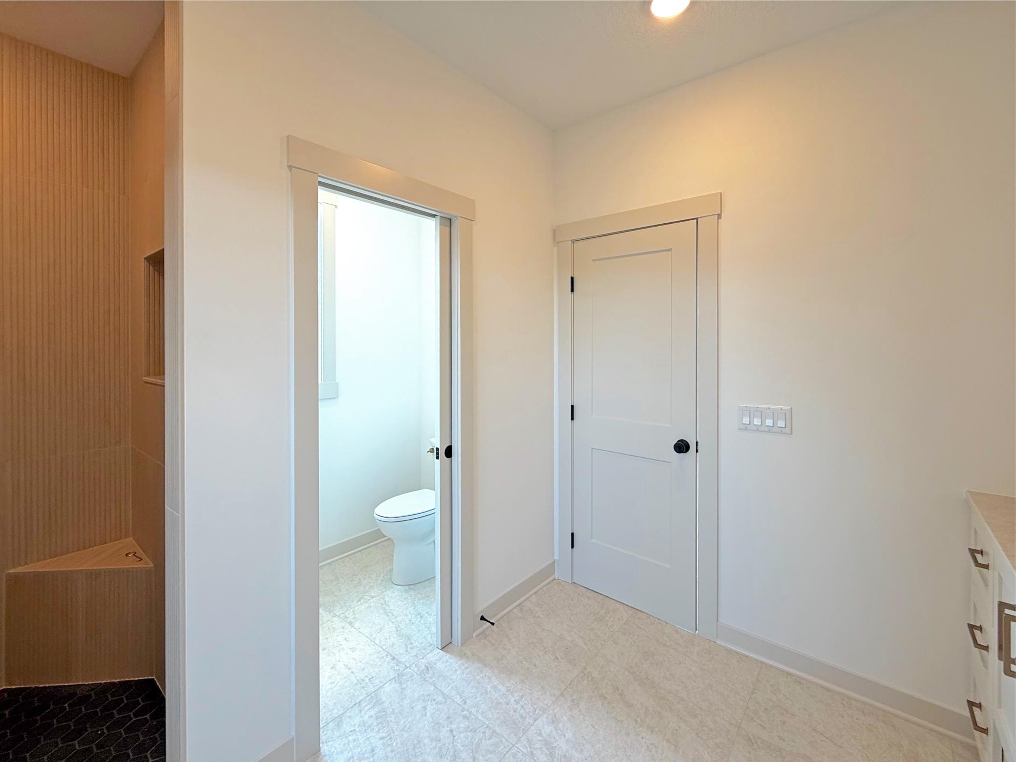 The primary bathroom features a private water closet and an oversized walk-in shower with custom tile, warm wood accents, and a built-in bench for a true spa-like experience.