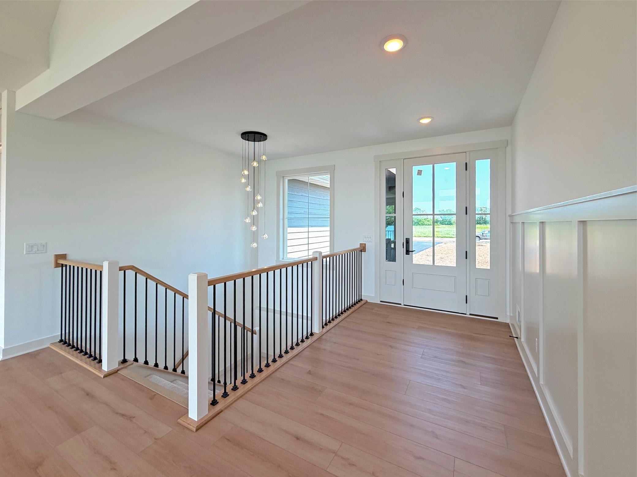 An inviting foyer welcomes you with its soaring ceiling, wood floors, decorative walls, designer lighting, and open staircase showcasing timeless craftsmanship and modern elegance.