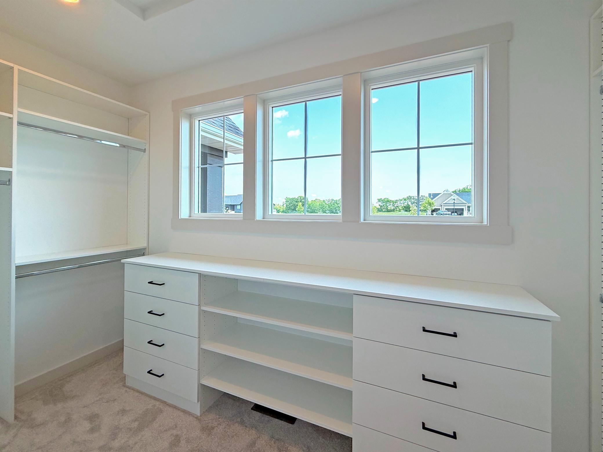 Designed with organization in mind, the spacious walk-in closet features a built-in wardrobe system with generous drawers, shelving, and hanging space, all illuminated by natural light.