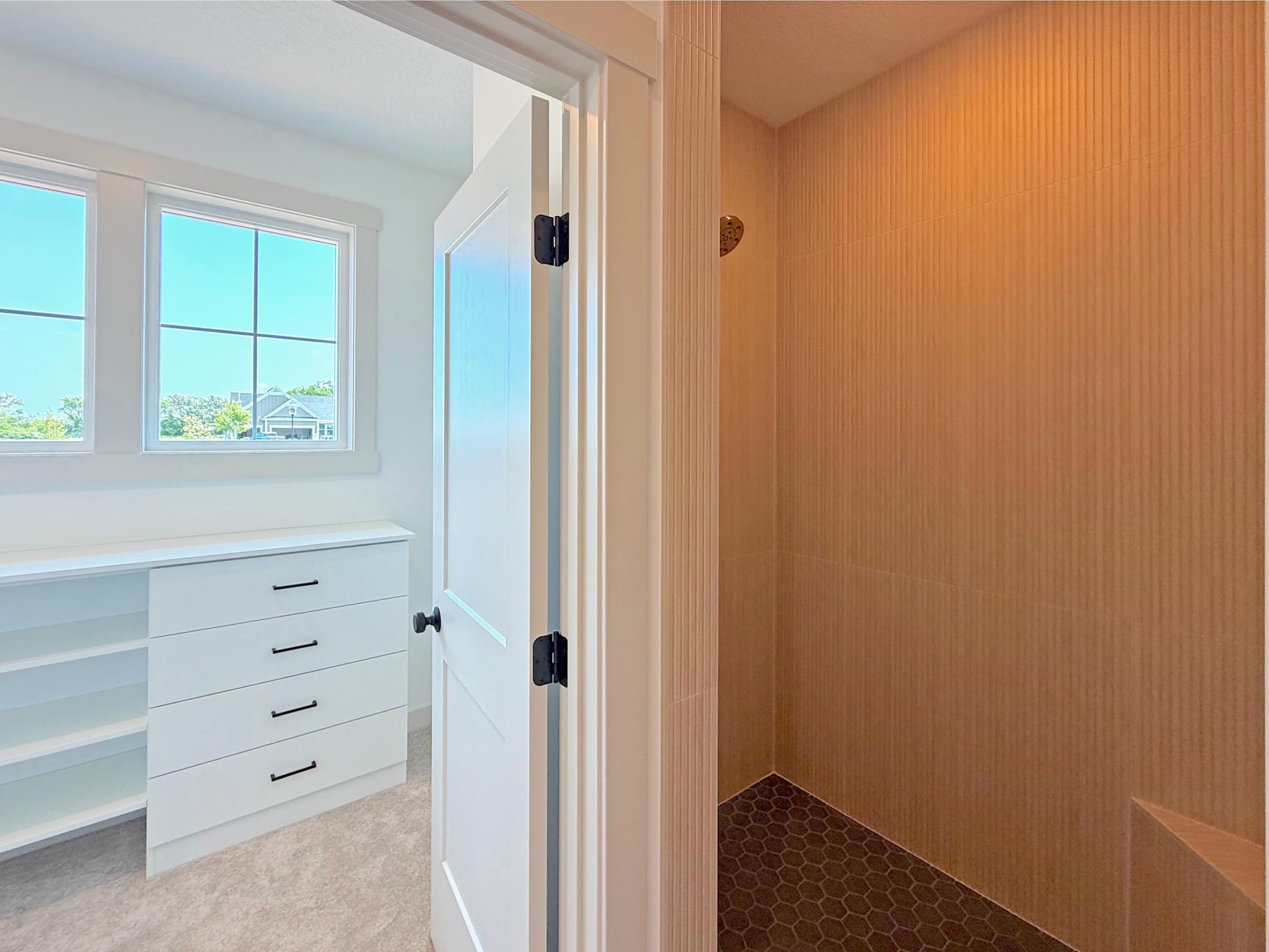 A stunning walk-in shower creates a true spa-like retreat with an adjoining custom walk-in closet is thoughtfully designed with built-in drawers, shelving, and generous storage.