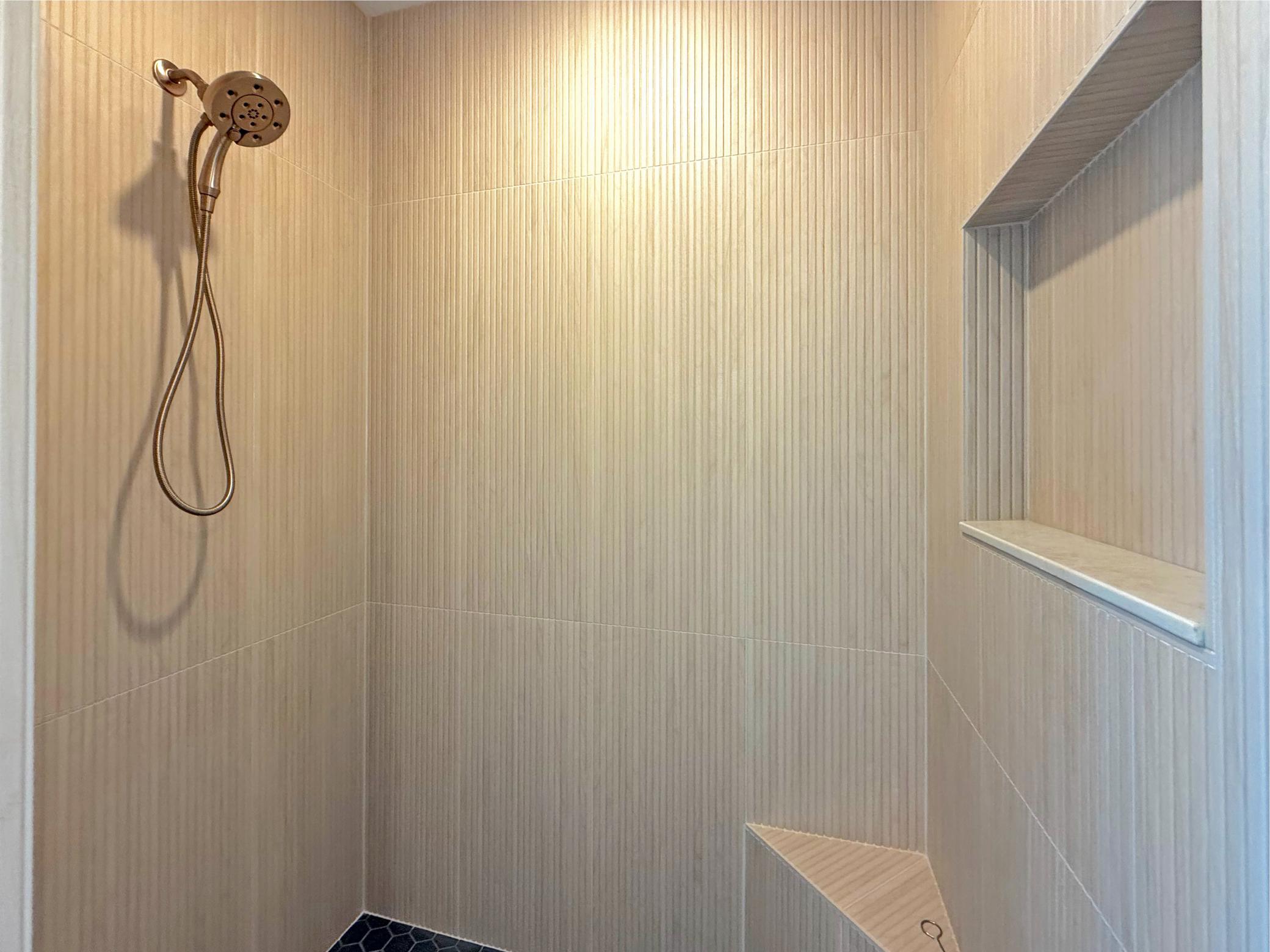 A striking combination of textured tile, warm neutral tones, and custom built-ins gives this walk-in shower a refined, spa-inspired feel that complements the home's modern lakeside aesthetic.