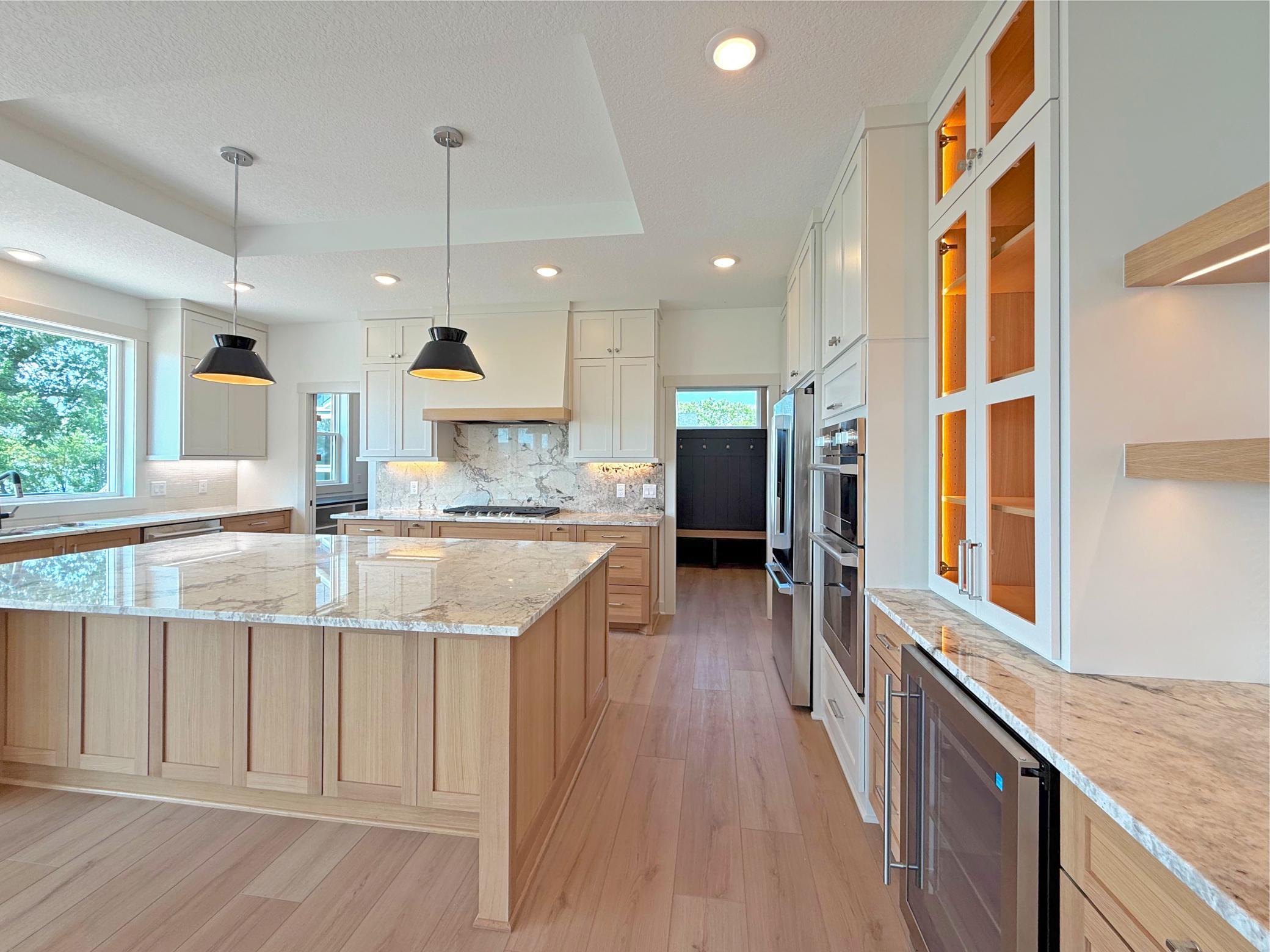 Thoughtfully designed with custom cabinetry, illuminated glass display cabinets, a built-in beverage refrigerator, floating wood shelves, this kitchen blends elegance with everyday convenience.