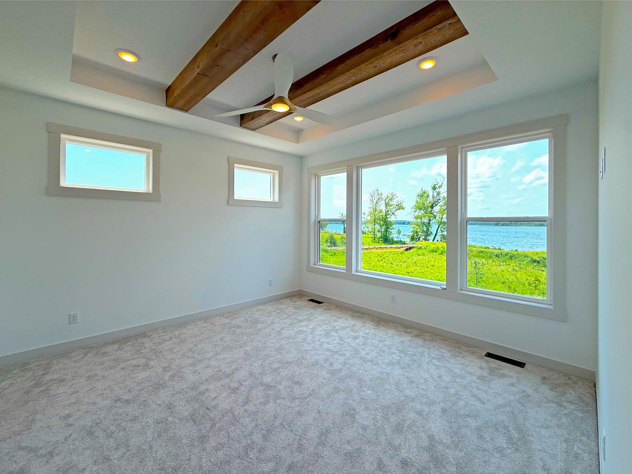 The spacious primary suite is designed as a peaceful retreat, featuring a striking box-vault ceiling with exposed wood beams and expansive windows that frame beautiful lake views.