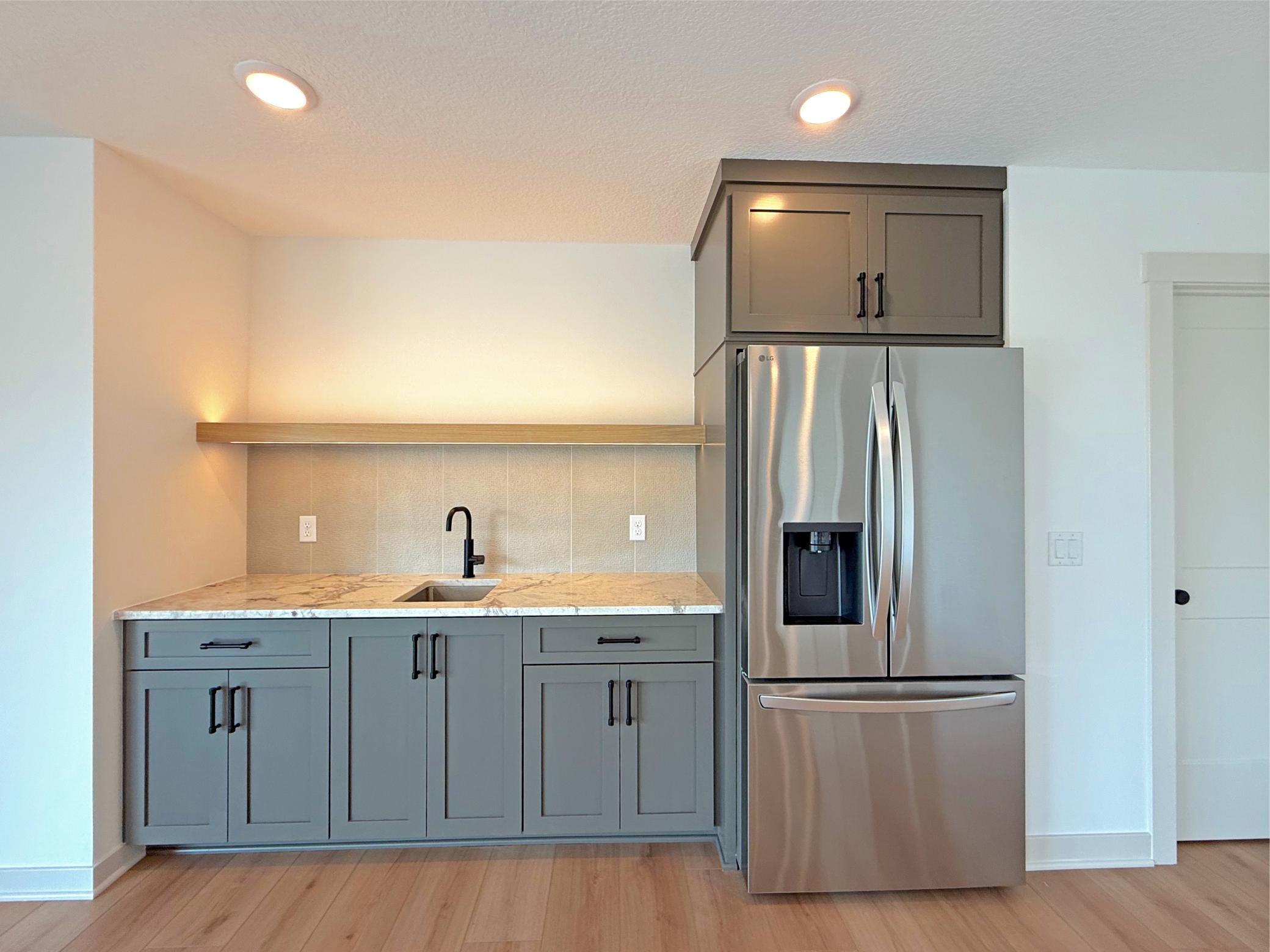 Perfect for hosting, the stylish wet bar features custom cabinetry, quartz countertops, a refrigerator, floating wood shelf, and sink - creating a convenient space for serving drinks and snacks.