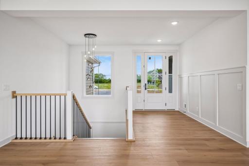 An inviting foyer welcomes you with its soaring ceiling, wood floors, decorative walls, designer lighting, and open staircase showcasing timeless craftsmanship and modern elegance.