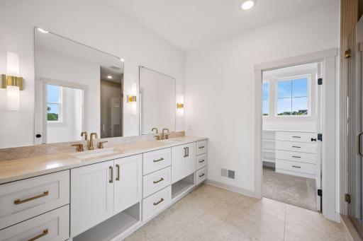 The thoughtfully designed primary bathroom features a spacious dual-sink vanity with quartz countertops, bright custom cabinetry & flooring, soft lighting and elegant finishes.