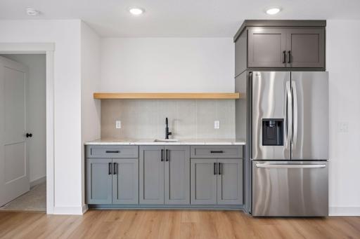 Perfect for hosting, the stylish wet bar features custom cabinetry, quartz countertops, a refrigerator, floating wood shelf, and sink - creating a convenient space for serving drinks and snacks.