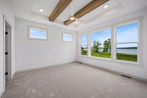 The spacious primary suite is designed as a peaceful retreat, featuring a striking box-vault ceiling with exposed wood beams and expansive windows that frame beautiful lake views.