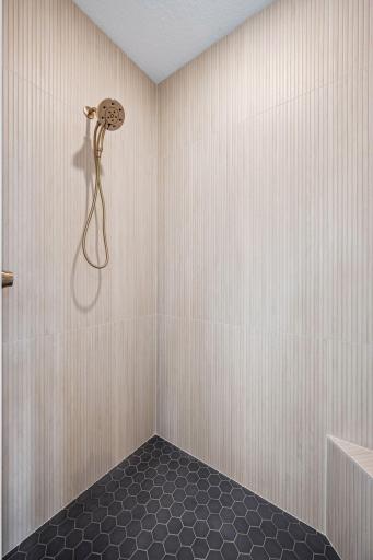 A striking combination of textured tile, warm neutral tones, and custom built-ins gives this walk-in shower a refined, spa-inspired feel that complements the home's modern lakeside aesthetic.