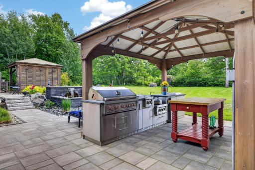 Outdoor kitchen with grill, cooktop, sink, and refrigerator.