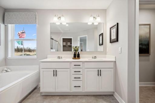 An extension of the primary suite, this private and spacious bathroom contains a double-vanity, a separate shower and tub, a private water closet, plus two walk-in closets. Photo is of previously built model home, finishes, selections will vary.
