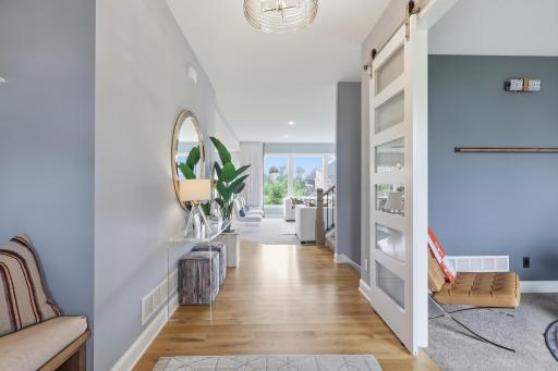 A welcoming foyer with a built in bench on the left and greeted by gleaming solid wood floors. Note the sliding barn door to the office on the right.