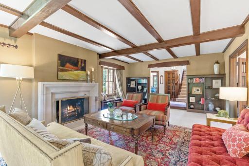 Living room rich with character: wood-burning fireplace with limestone surround, bay window, exposed wood beams and built-in bookshelves