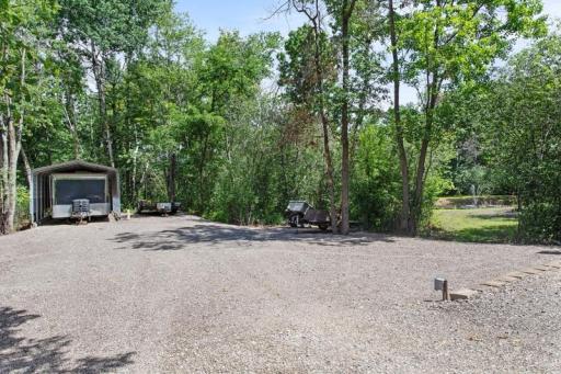 Large parking area and car port behind building with a trail leading to a portion of the property behind the home