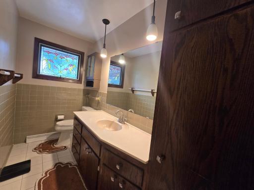 Full main floor bathroom with tile floors, walls and stained glass windows and easy clean counter tops with lots of linen storage plus a large built in cabinet in the hallway.