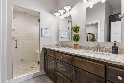 The beautifully finished lower-level bathroom includes a double vanity, tiled steam shower, and rain shower feature.