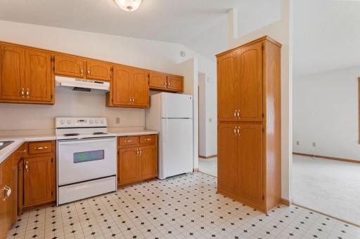 Unstaged view highlighting the kitchen's efficient walk-through design and exceptional storage, including a large pantry cabinet and extensive cabinetry in excellent condition.