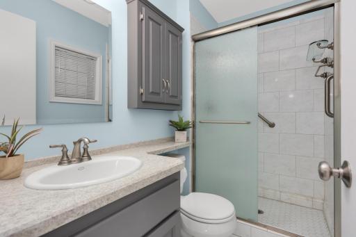 Updated primary bathroom features a tiled walk-in shower, modern vanity, and additional storage.
