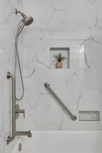 Stylish tub and shower surround with built-in niche, grab bars, and elegant tilework.