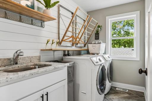Convenient upper level laundry room featuring utility sink, granite counters, and tiled floors.