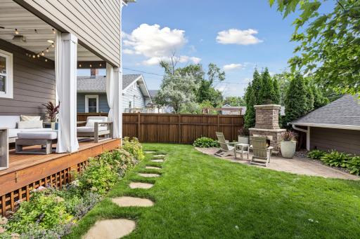 Beautifully landscaped backyard featuring a patio, custom outdoor fireplace, and privacy fencing, ideal for relaxing or entertaining.