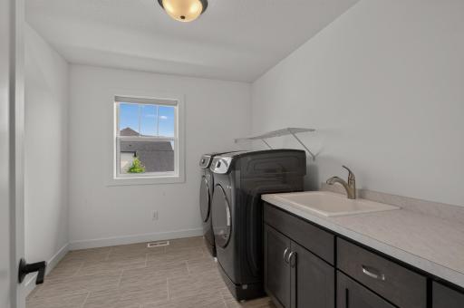 Keep household tasks organized with a roomy upper level laundry area featuring built-in cabinetry, a utility sink, generous counter space, and a bright window.