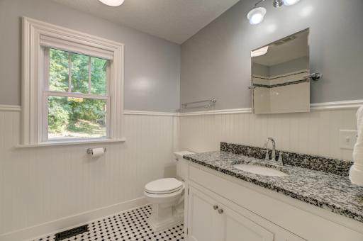 Main level bathroom with wainscoting, granite vanity top, and ceramic tiled floor and tub surround.