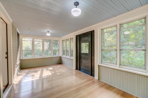 Spacious front porch interior with maple floors and wainscoting below the windows.