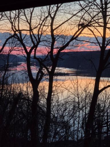 Views of a sunrise over the river when leaves are off the trees.