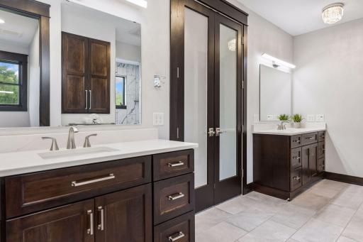 Primary bathroom Features - Frosted double doors, Three mini chandeliers 3000k light temp, Symmetrical men’s and women’s counters, toilet rooms, and shower space.