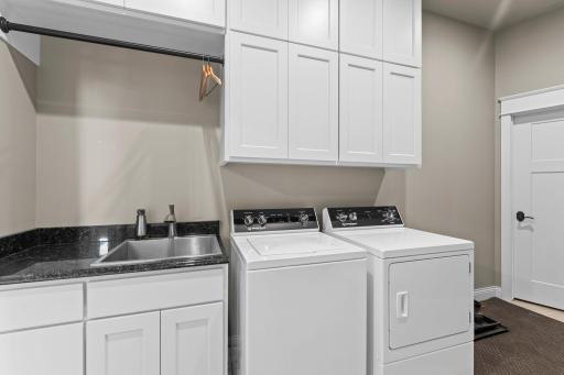 Main level laundry with finished cabinetry, a granite countertop, and a stainless utility sink, offering a well-organized and functional space for everyday household tasks. Located on the main floor for convenient access and pocket door entry.