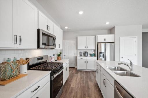 A stunning Kitchen with white cabinets, accented black hardware, quartz counters, and tiled backsplash. Photo of model home , colors and finishes will vary.