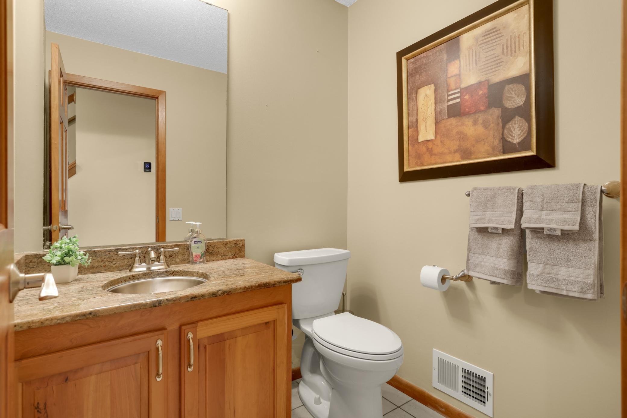 Conveniently located half bath on main level with granite countertop, stainless steel sink, and wood cabinetry.