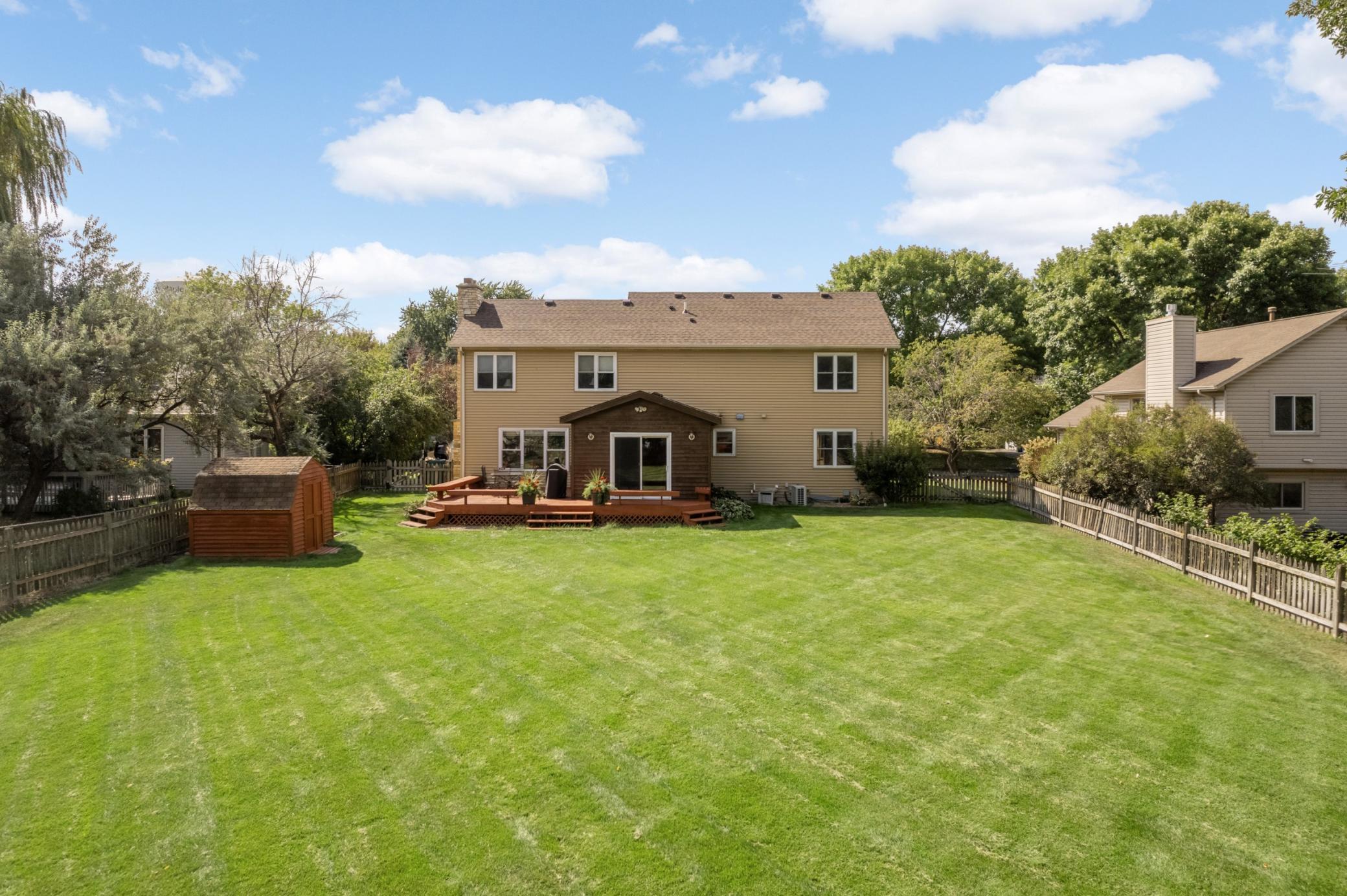 Expansive fenced backyard with a spacious deck and two storage sheds.