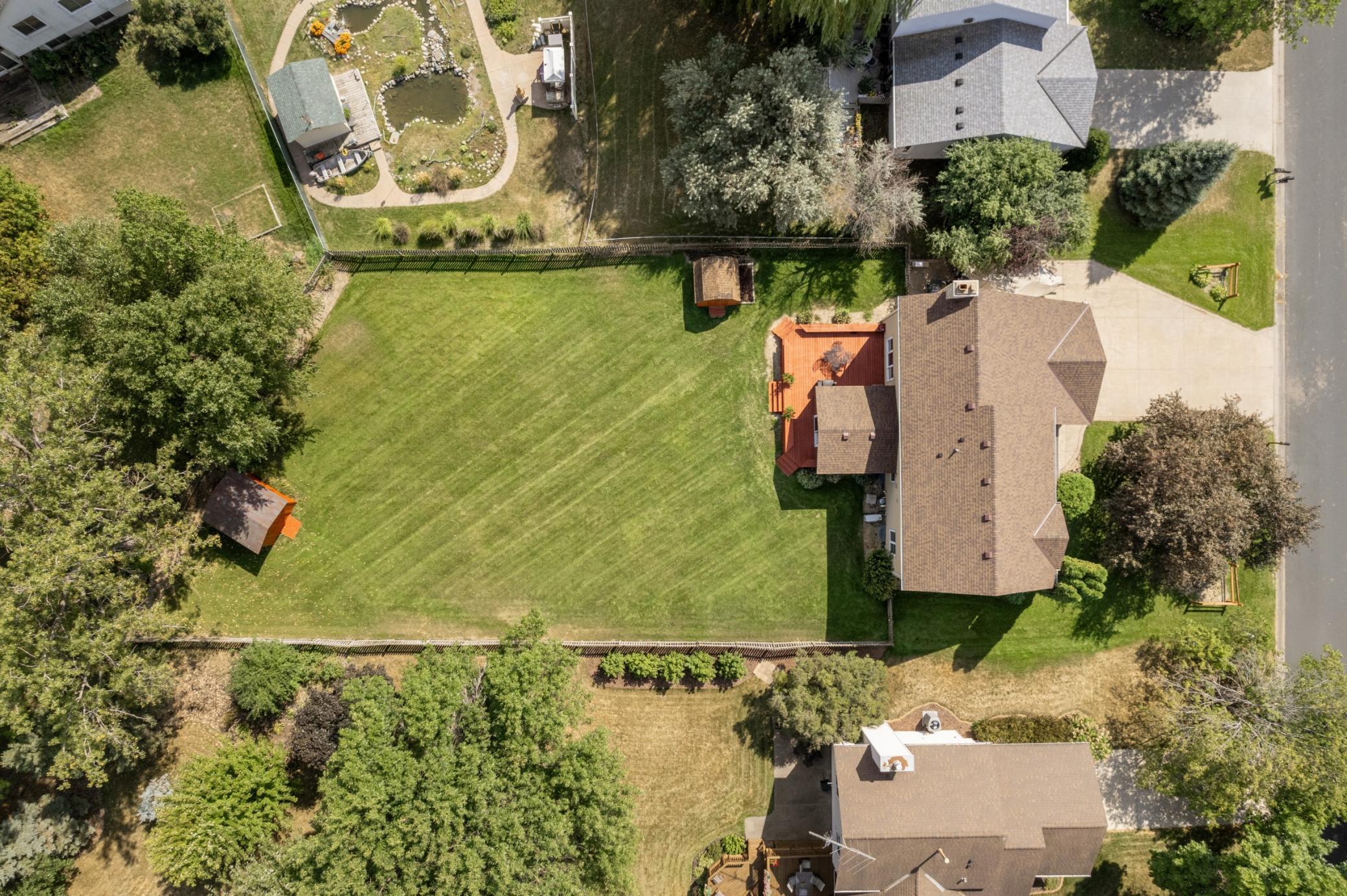 Expansive fenced backyard with a spacious deck, mature trees and two storage sheds.