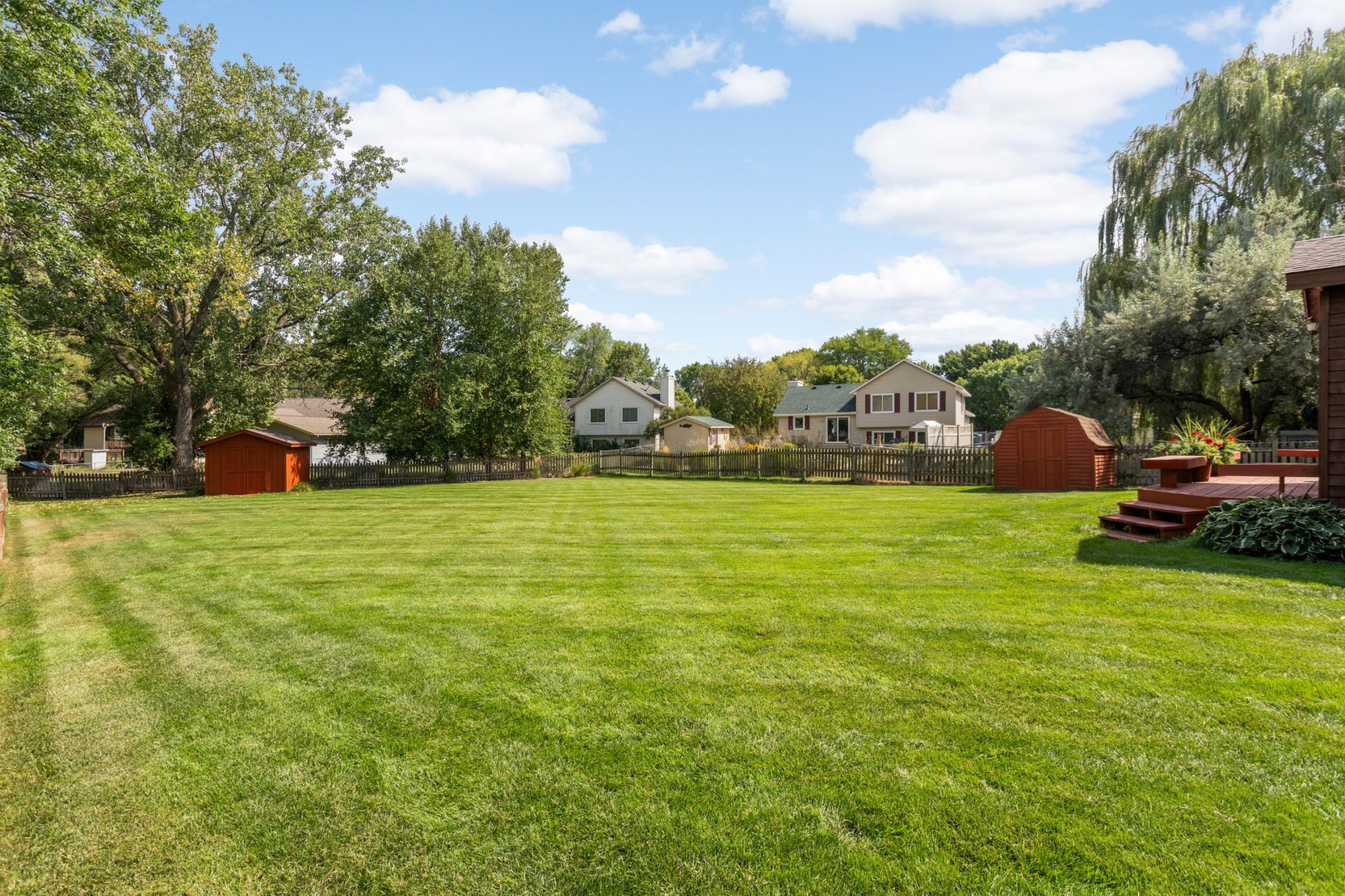 Expansive fenced backyard with a spacious deck, and two storage sheds.
