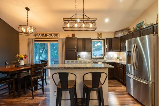 The kitchen has granite countertops, stainless steel appliances, vinyl plank flooring, under cabinet lighting, tile backsplash, updated light fixtures, breakfast bar and the sink overlooks the backyard.