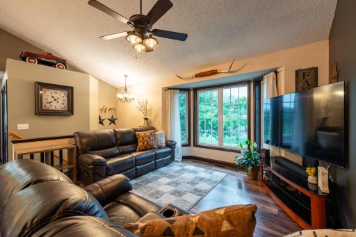 The living room features vinyl plank flooring, ceiling fan, vaulted ceiling and bay window overlooking the front yard.