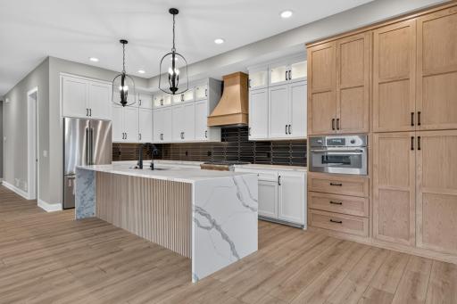 A balanced mixture of enameled & white oak cabinetry features flat panel & glass doors w/ interior accent lighting, roll-out storage, full height pantry, under cabinet lighting and an oversized âEat-Inâ center island w/ modern wood paneled front