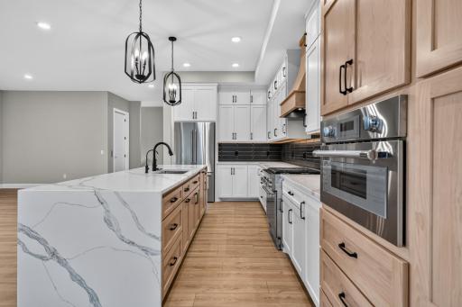 High-end Thermador stainless steel appliances include a French door refrigerator, gas cooktop with decorative wood paneled hood, wall oven and cabinet paneled dishwasher