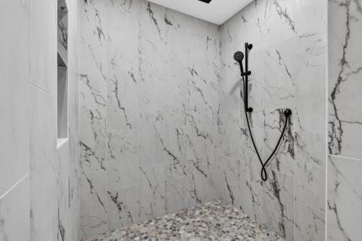 Custom tile shower features modern tile surround, shampoo niche, stone pebble base and additional hand shower