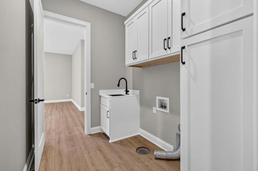 Laundry Room features enameled cabinetry with quartz countertop and stainless steel utility sink