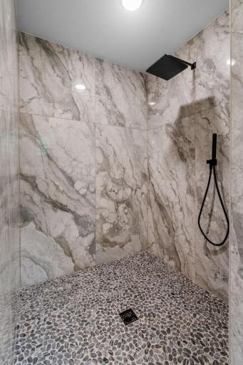 Custom tile shower features a large scale polished marble tile surround, stone pebble base and a handshower