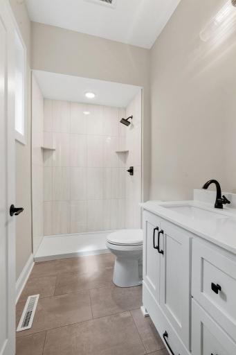 Private 3/4 bathroom features enameled vanity cabinet w/ quartz countertop, modern tile flooring and natural light. Shower features a ceramic tile surround
