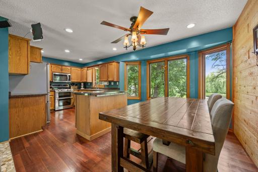 Bright kitchen and dining area featuring warm wood cabinetry, a center island. and large windows showcasing outdoor views.