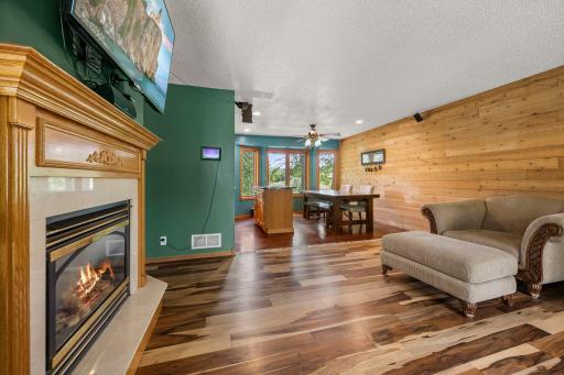 Warm and inviting living room featuring a cozy fireplace, and a rustic wood accent wall, flowing seamlessly into a bright dining area with views of the backyard.