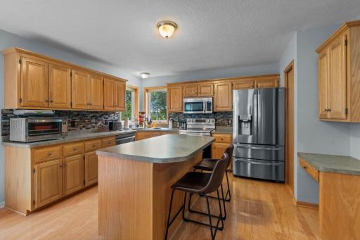 Designed for both cooking and gathering, the kitchen features hardwood floors, stainless steel appliances, a tile backsplash, and a center island with extra seating